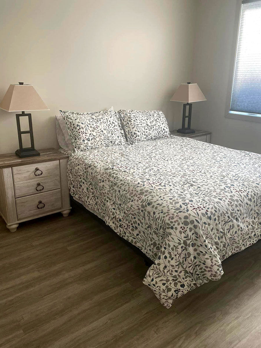 Guest suite at Kinsmen Kourts II, featuring a queen sized bed with comfy pillows and comforter, night tables, and private bathroom.