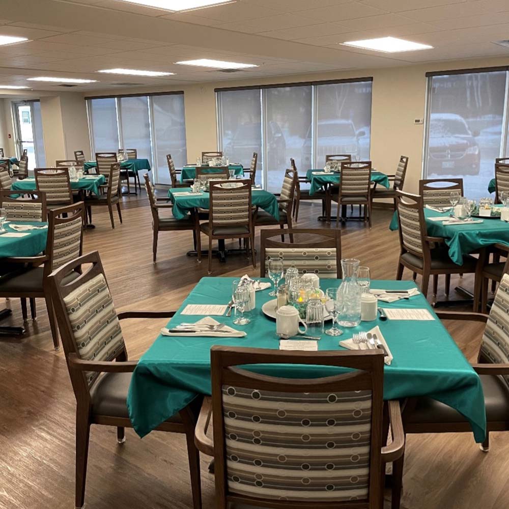 Dining room at Kinsmen Kourts 2 in Neepawa, Manitoba. A number of tables are set with teal table cloths. Each table has four wood and upholstered chairs.