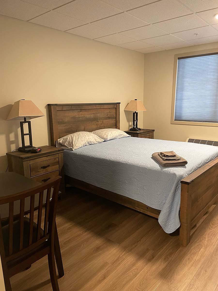 Main floor guest room at Kinsmen Kourts 2, featuring a queen sized bed with comfy pillows and comforter, night tables, and private bathroom.